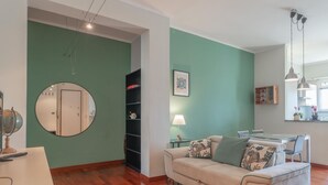 A living room with a round mirror, a sofa with patterned cushions, a dining table, and a bookshelf. - [AC] La Finestra Sulla Mole (Torino)