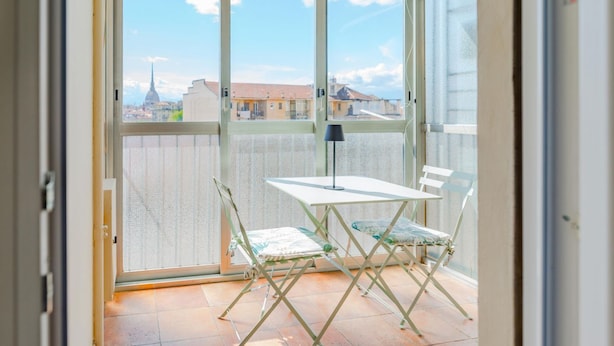 A balcony with a table and chairs, a view of buildings, and a clear sky. - [AC] La Finestra Sulla Mole (Torino)