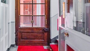 A hallway with a wooden door, a red carpet, and a window with a metal grid. - Ca' Vittoria by HappyHosTorino (Torino)