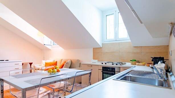 A modern kitchen with a central island, a dining area with a glass table, and a cozy seating area with a sofa and cushions. - Ca' Vittoria by HappyHosTorino (Torino)