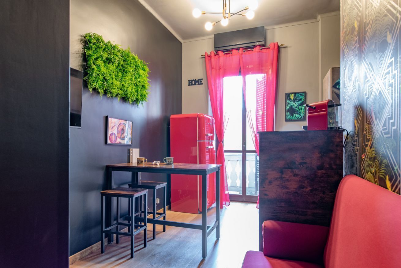 A modern kitchen with a dining area, a red sofa, and a green wall decoration.