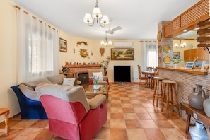 Een woonkamer met een bank, televisie, open haard en een eethoek met stoelen en een bar.