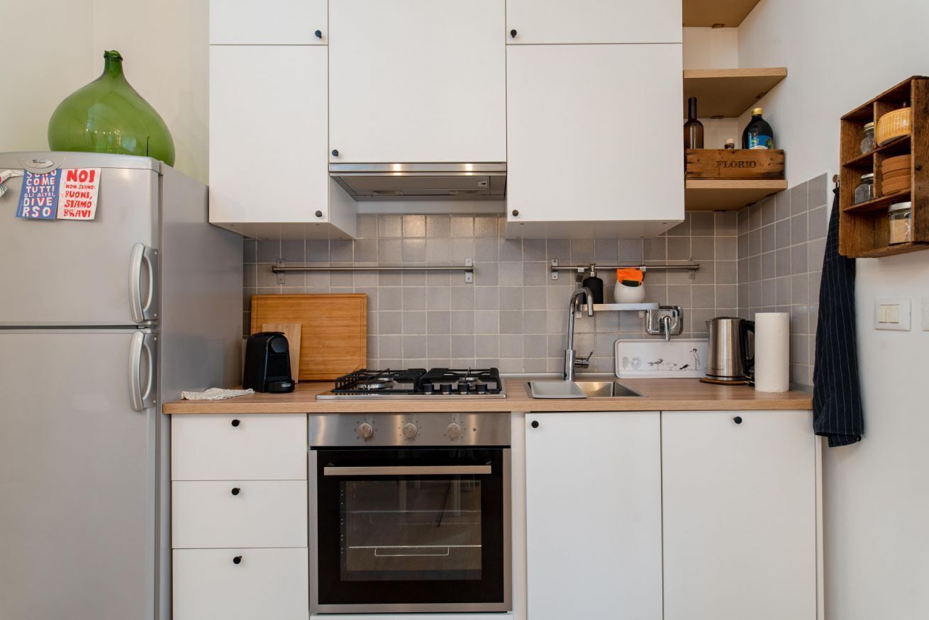 A compact kitchen with white cabinets, a gas stove, a built-in oven, a coffee maker, and a wooden cutting board.