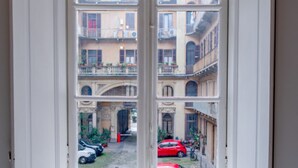 Blick durch ein Fenster auf einen Innenhof mit Gebäuden, einem roten Auto und einem weißen Auto.