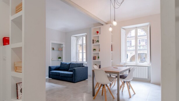 Ein modernes Wohnzimmer mit einem blauen Sofa, einem Esstisch mit Stühlen und einem Bücherregal.