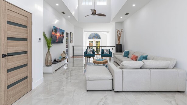 A spacious living room with a large sectional sofa, a ceiling fan, and a view of the outdoors through a large window. - Avion Park Luxury Home | Waterfront • Private Dock • Modern 3BR Naples (Naples)