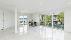 A spacious, modern living room with a large glass door leading to a balcony, a dining area with a table and chairs, and a view of the outdoors. - Avion Park Luxury Home | Waterfront • Private Dock • Modern 3BR Naples (Naples)