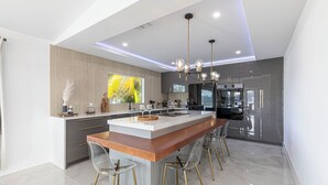 A modern kitchen with a central island, bar stools, and a large window. - Avion Park Luxury Home | Waterfront • Private Dock • Modern 3BR Naples (Naples)