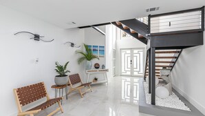 A modern interior with a staircase, two wooden benches, a potted plant, and a decorative wall piece. - Avion Park Luxury Home | Waterfront • Private Dock • Modern 3BR Naples (Naples)