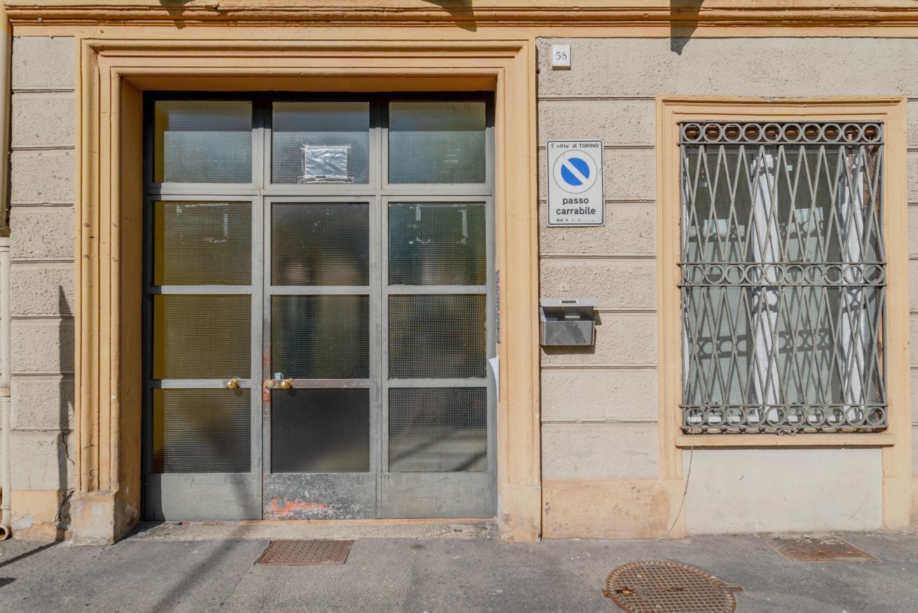 L'ingresso di un edificio con un cancello in metallo, una finestra dotata di inferriata e un cartello che indica divieto di sosta.