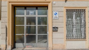 Entrada de um edifício com portão de metal, janela com grade e placa de proibido estacionar.