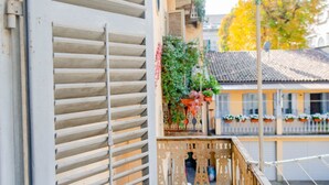 A balcony with a metal railing, a window with horizontal blinds, and a view of a building with a tiled roof and potted plants. - [Centro, elegante]: The Queen by HappyHosTorino* (Torino)