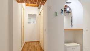 Ein Korridor mit Holzboden, weißen Wänden und einer Ziegeldecke. Es gibt einen weißen Schrank mit Griff und ein kleines Regal mit einem Bilderrahmen.
