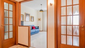 Un pasillo que conduce a una sala de estar con un sofá azul, cuadros en la pared y una lámpara en el techo.