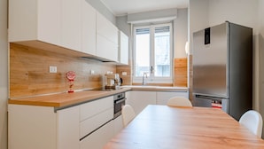 Een moderne keuken met witte kasten, een houten aanrecht, een roestvrijstalen koelkast, en een eetgedeelte met een houten tafel en stoelen.