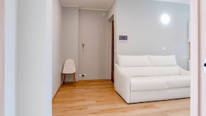 Een kamer met een witte bank, een houten vloer en een witte stoel.
