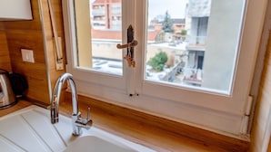 Een keuken met een wit spoelbak, een roestvrijstalen kraan en een raam met uitzicht op gebouwen.