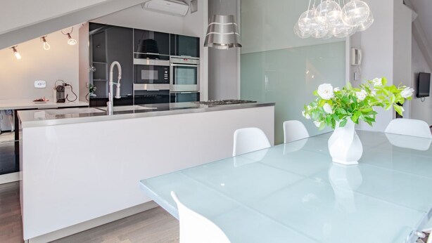 A modern kitchen with stainless steel appliances, a glass island, and white chairs. - La Terrazza sui Tetti (Torino)