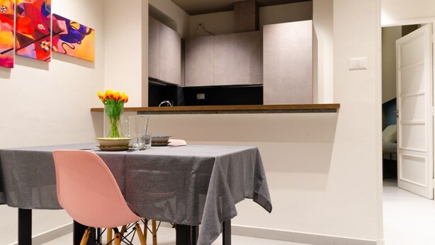 A dining area with a table set for two, a vase of flowers, and abstract art on the wall. - [AC, Centralissimo] Bertola by HappyHosTorino (Torino)