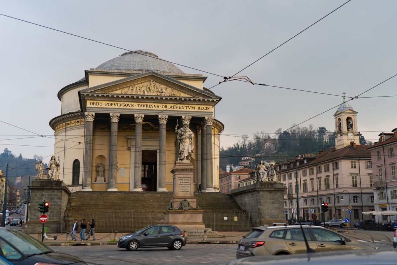 Un bâtiment de style classique, doté de colonnes et d’un dôme, entouré de rues et d’immeubles de la ville.