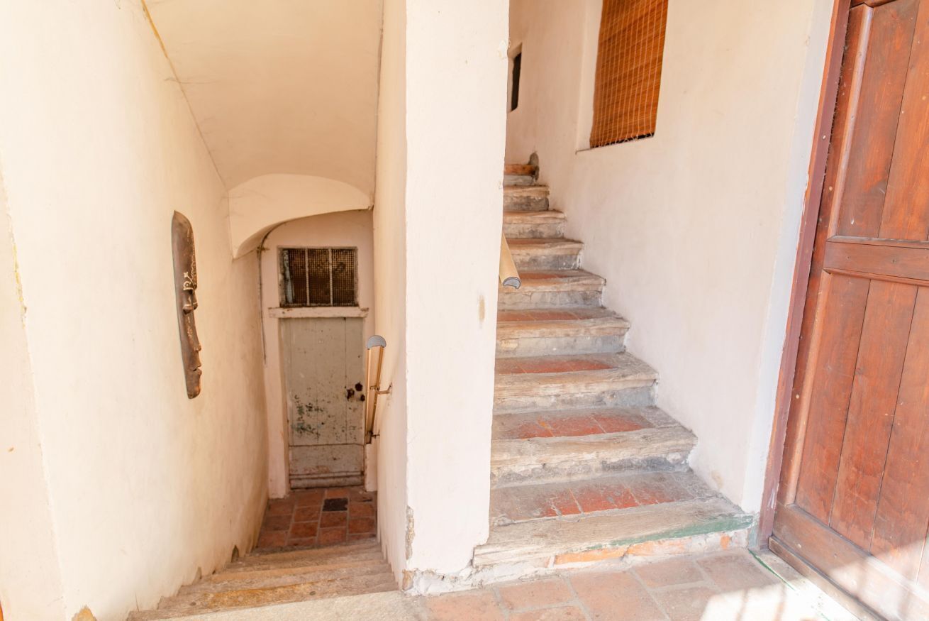 A narrow stairway leading to a door with a metal gate, flanked by white walls and a wooden door on the right.