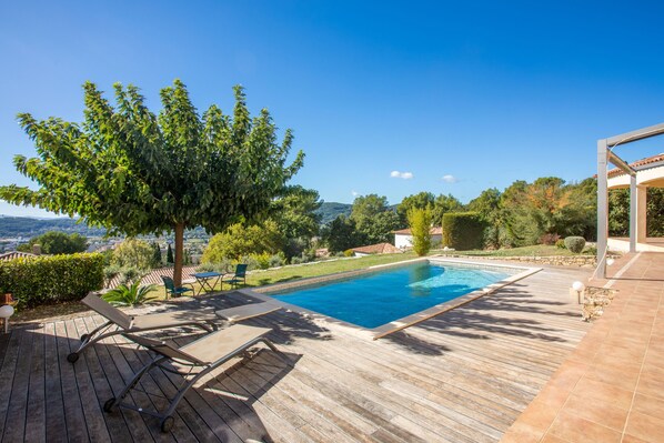 Une terrasse en bois avec une piscine, des chaises longues et une pergola.