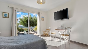 A bedroom with a bed, a TV, a table with chairs, and a view through a sliding door.