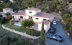 Une maison à deux étages avec une piscine, des voitures garées et un mur de pierre qui entoure la propriété.