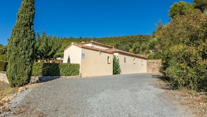 A single-story building with a tiled roof, a gravel driveway, and a clear blue sky.