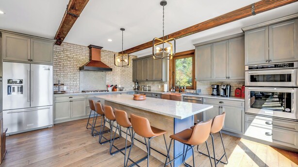 Una cocina moderna con una isla grande, taburetes de bar, electrodomésticos de acero inoxidable y vigas de madera a la vista.