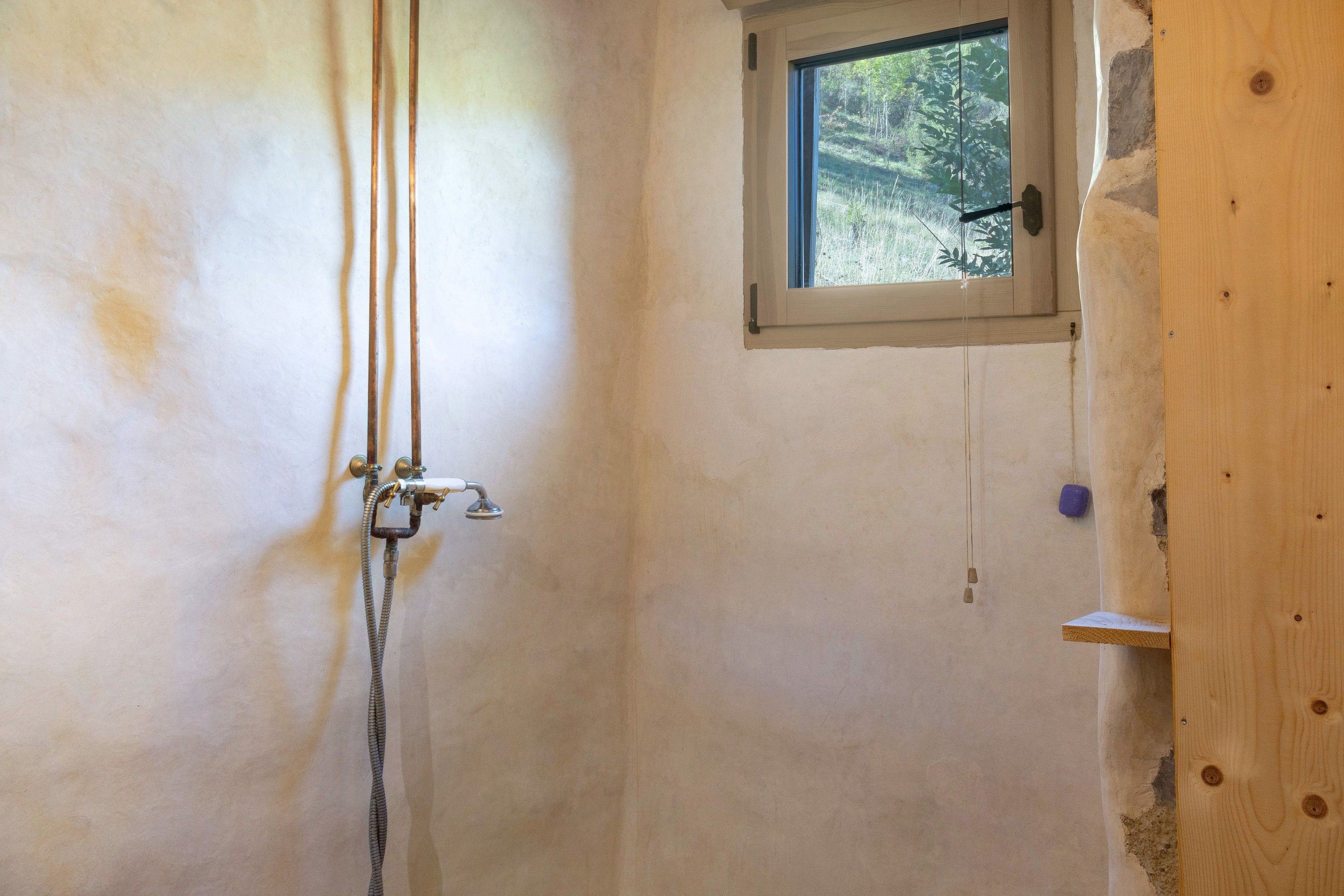 Een badkamer met een douche, een raam en zichtbare leidingen.