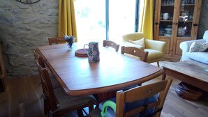 A dining area with a wooden table, chairs, a clock on the wall, and a view through the window. - Ferme des Montagnes Bleues – Guest Room with Breakfast in the Peaceful Drôme Mountains (Bellegarde-en-Diois)