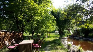 A rustic outdoor seating area with a wooden table and chairs, surrounded by lush greenery and a small stream. - Ferme des Montagnes Bleues – Guest Room with Breakfast in the Peaceful Drôme Mountains (Bellegarde-en-Diois)