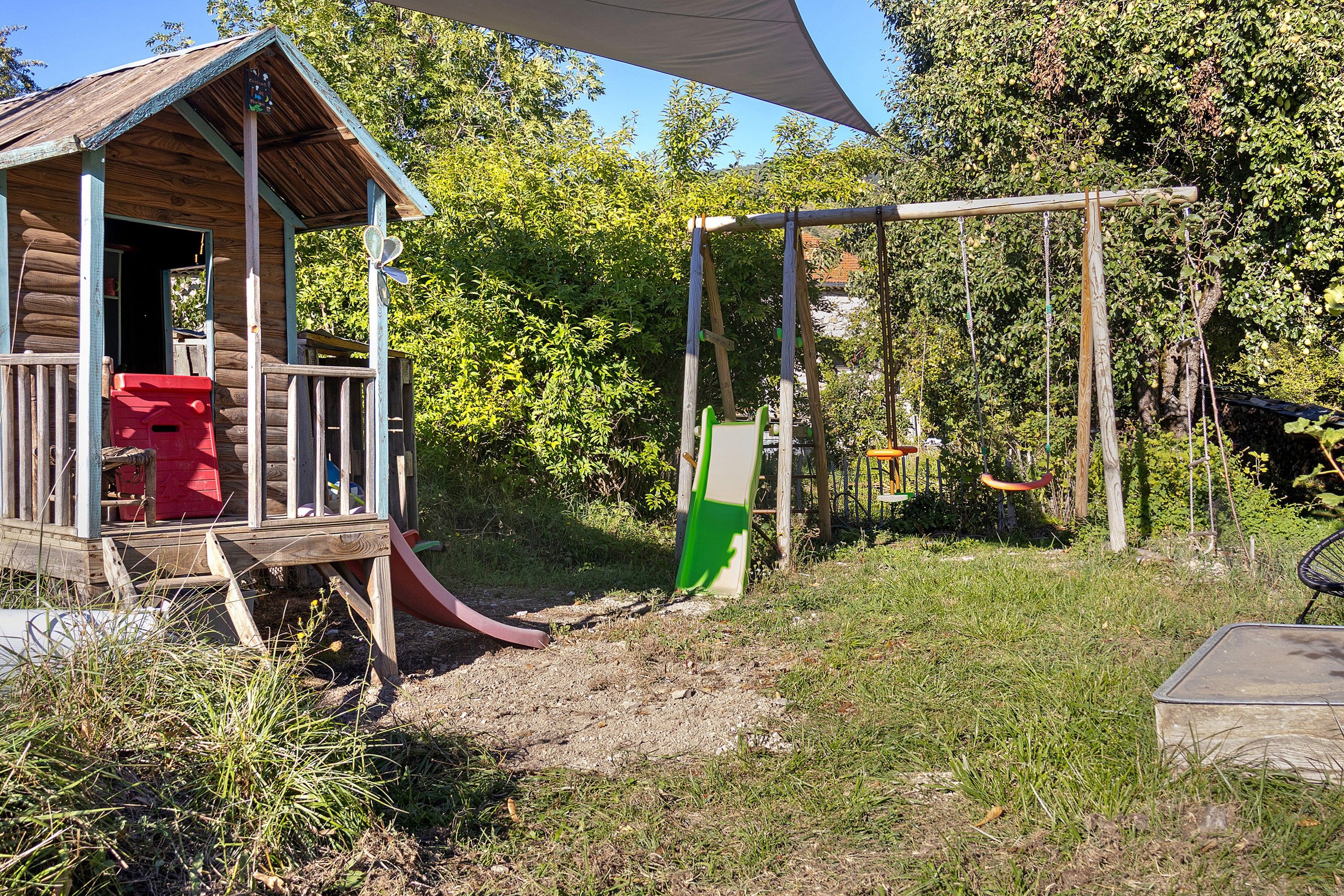 Une cabane en bois avec un toboggan, entourée d’arbres et d’une pelouse.