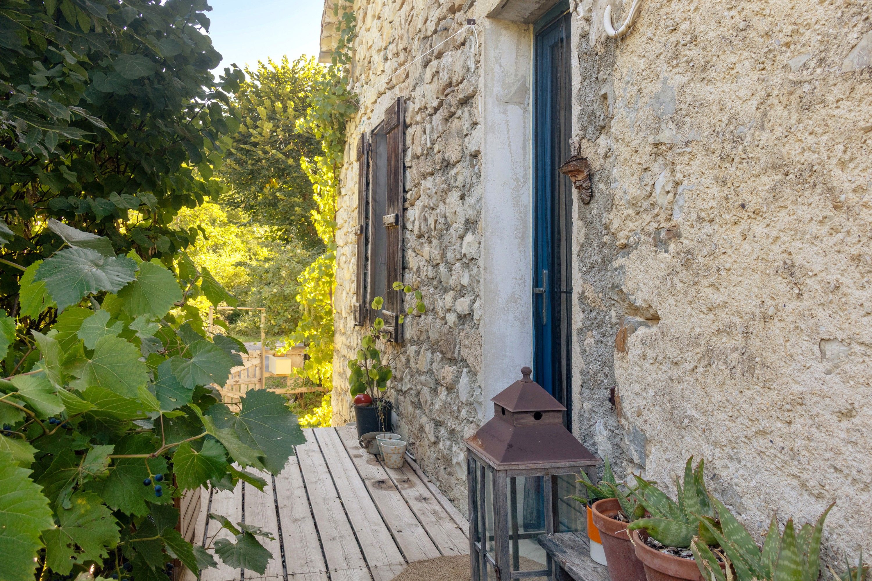 Un bâtiment en pierre doté d’une terrasse en bois, d’une lanterne et de plantes en pot.