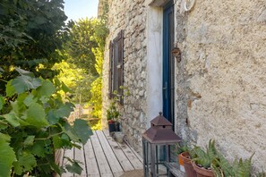 Un edificio de piedra con una terraza de madera, un farolillo y macetas con plantas.