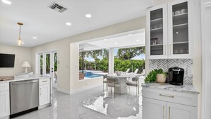 A modern kitchen with white cabinetry, a built-in dishwasher, and a coffee machine. - Gorgeous Modern Beach Heated Pool House Sleeps 8 Central (Delray Beach)