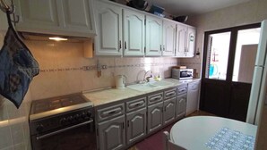 A compact kitchen with white cabinets, a stove, a sink, and a microwave. - Casa da Fatima in Angra do Heroismo (Angra do Heroismo)