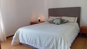 A neatly made bed with a striped bedspread, a decorative pillow, a bedside table with a lamp, and a small stool. - Casa da Fatima in Angra do Heroismo (Angra do Heroismo)