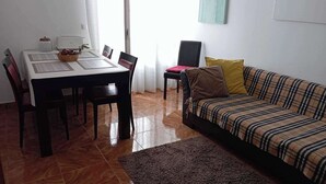 A dining area with a table and chairs, a sofa, a rug, and a window with curtains. - Casa da Fatima in Angra do Heroismo (Angra do Heroismo)