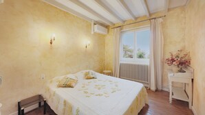 Ein Schlafzimmer mit Bett, einem Fenster mit Vorhängen, einem Heizkörper und einem kleinen Tisch mit einer Vase.