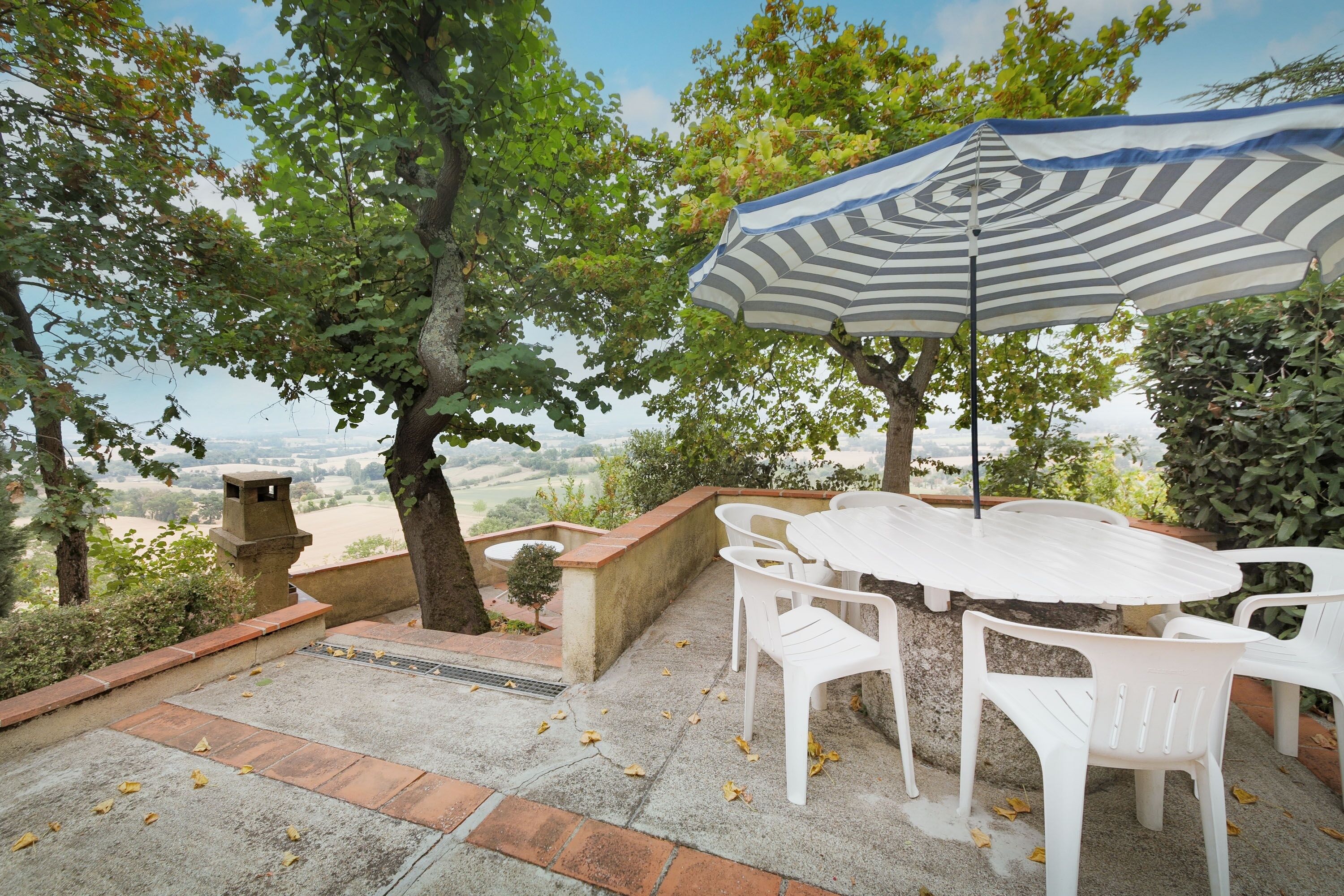 Une terrasse extérieure avec une table et des chaises, un parasol à rayures et une vue sur la campagne.