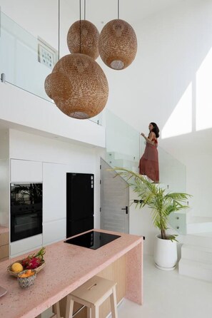 A modern kitchen with a pink countertop, black appliances, and a potted plant.