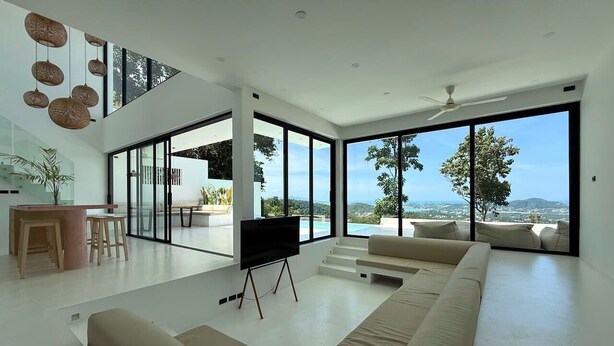 A modern living room with a large sectional sofa, a flat-screen TV on a stand, a dining area with a table and chairs, and large windows offering a view of the outdoors. - Palmaya Villa - Piscine & Vue mer - 3 chambres (Ko Samui)
