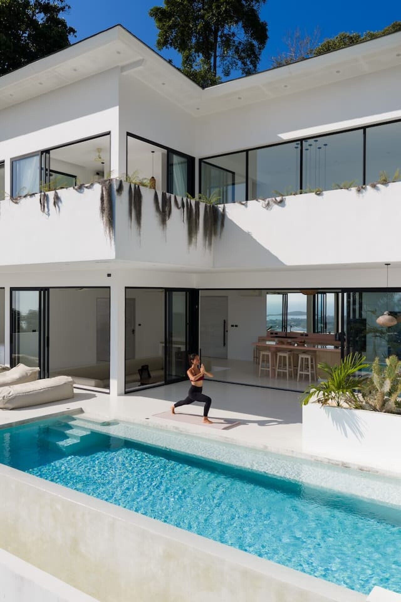 Ein modernes, zweistöckiges Haus mit Pool, großen Fenstern und Blick auf die Landschaft.