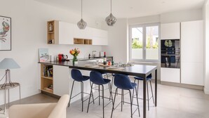 Een moderne keuken met een centraal eiland, barkrukken, hanglampen en uitzicht op het groen.