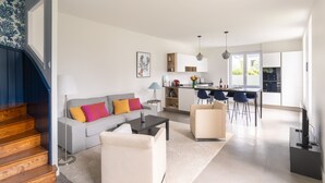 Een moderne woonkamer met een bank, salontafel en stoelen, een trap, een keuken met barkrukken en een eettafel.