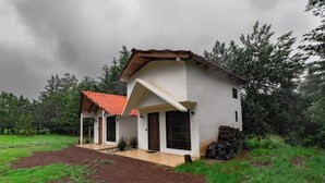 Una casa de dos plantas con techo de tejas rojas, un porche cubierto y un césped cuidado.