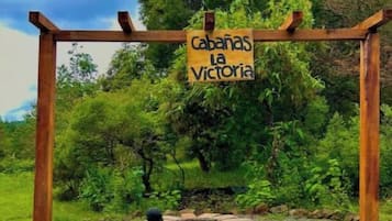 A wooden pergola with a sign reading "Cabanas La Victoria" in a natural setting with trees and grass.