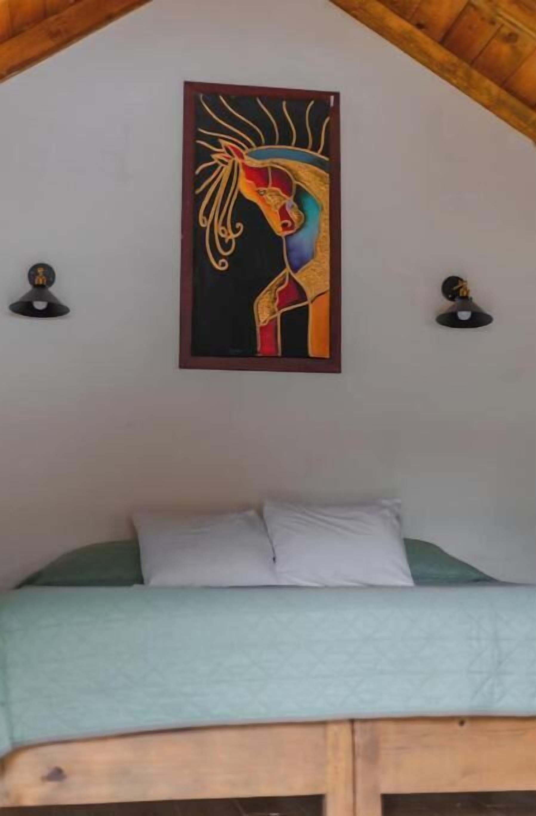 Een slaapkamer met een bed, een kunstwerk in een lijst erboven en twee wandlampen.